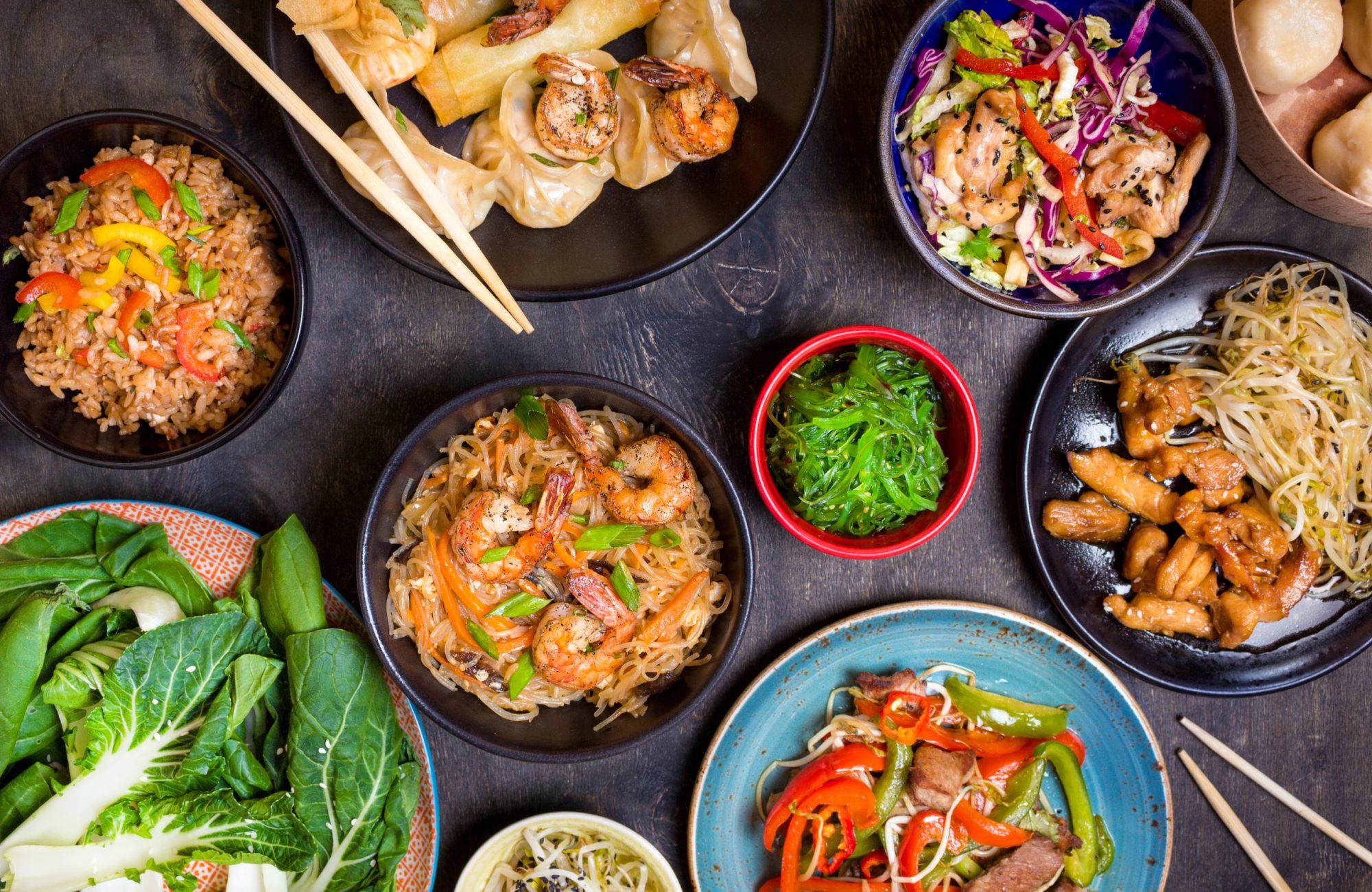 Chinese food on dark wooden table. Noodles, fried rice, dumplings, stir fry chicken, dim sum, spring rolls, bean sprouts, bok choy. Chinese cuisine set. Dinner party. Top view. Chinese restaurant